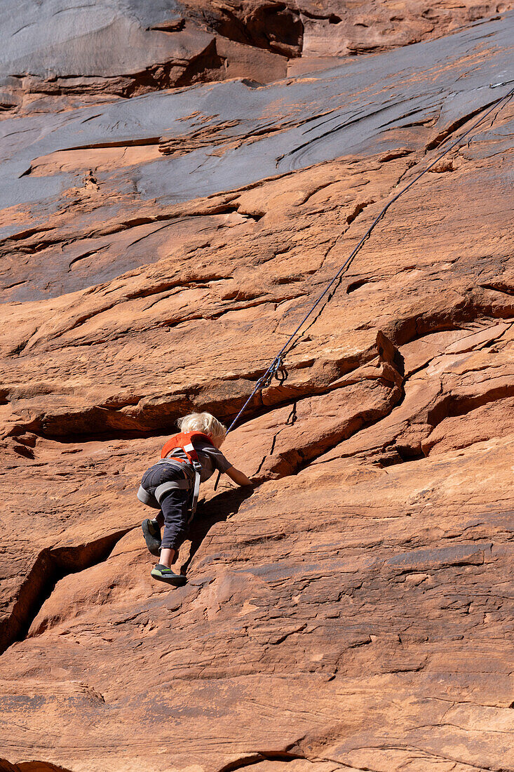 Ein kleiner Junge, 3 Jahre alt, lernt im Hunter Canyon in der Nähe von Moab, Utah, das Klettern.