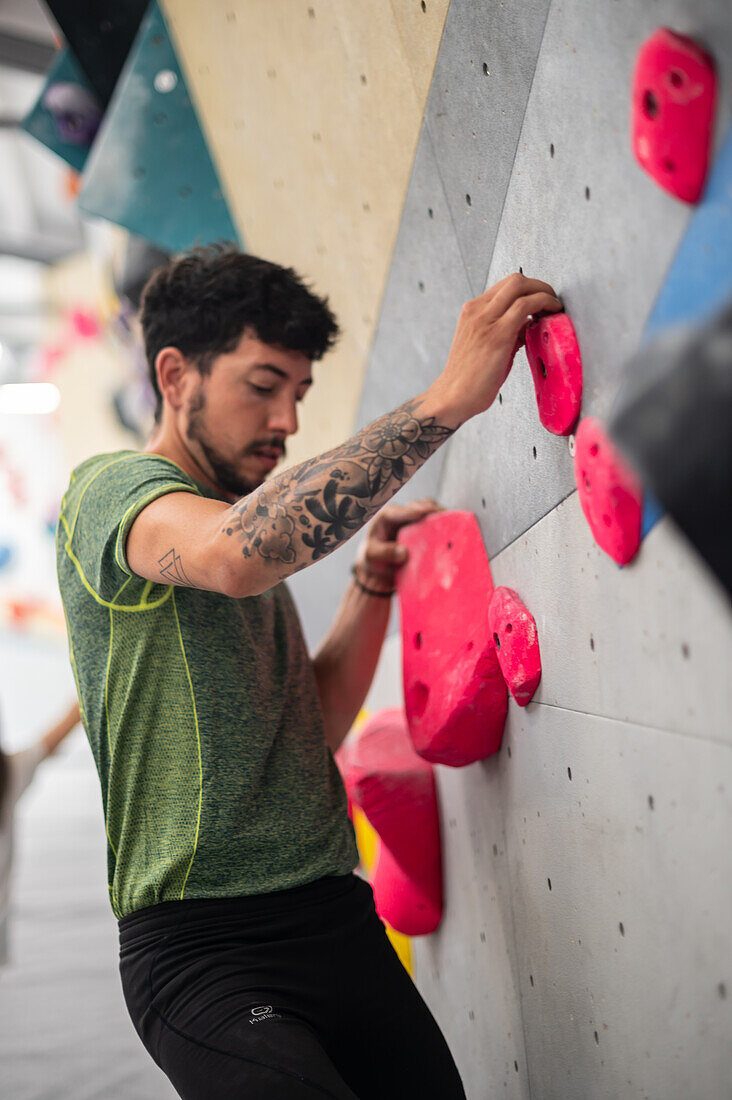 Junger Mann in den Zwanzigern beim Klettern an einer Kletterwand in einer Halle