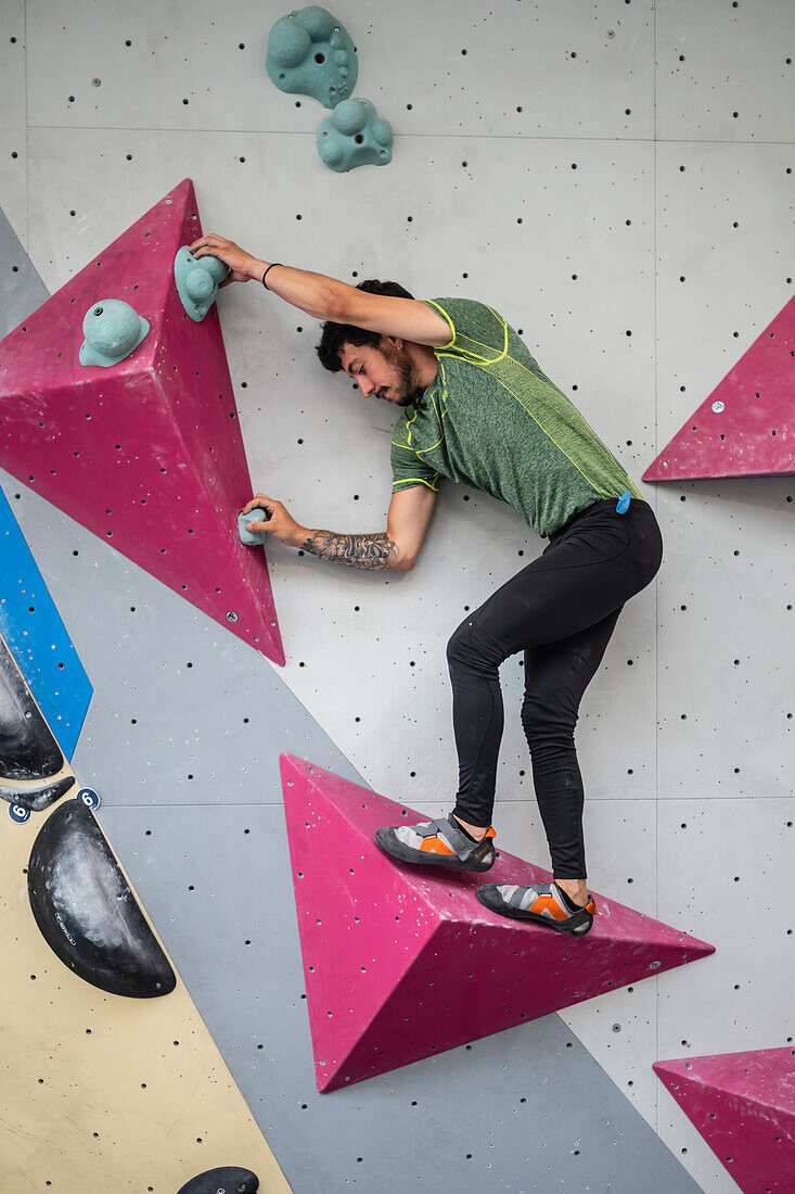 Junger Mann in den Zwanzigern beim Klettern an einer Kletterwand in einer Halle