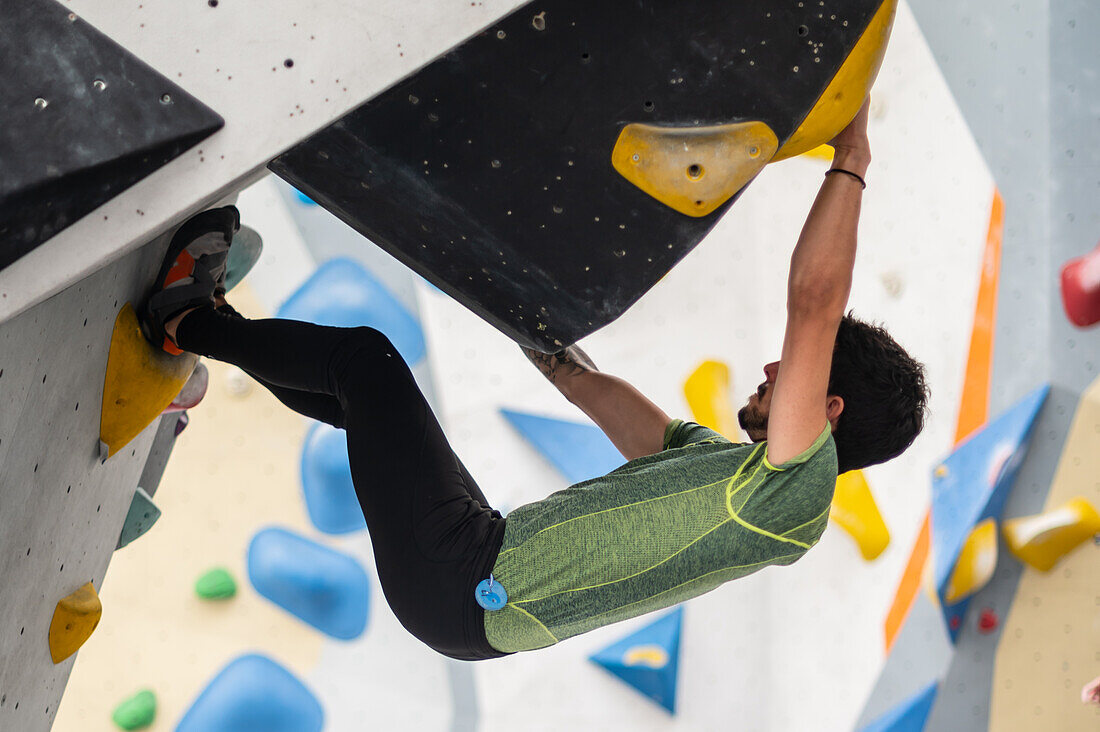 Young man in his twenties climbing on a climbing wall indoors