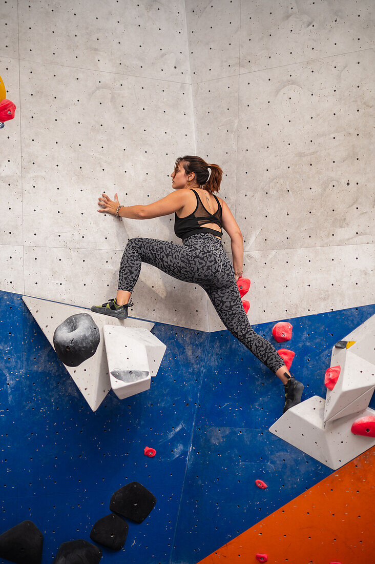 Young man in her twenties climbing on a climbing wall indoors