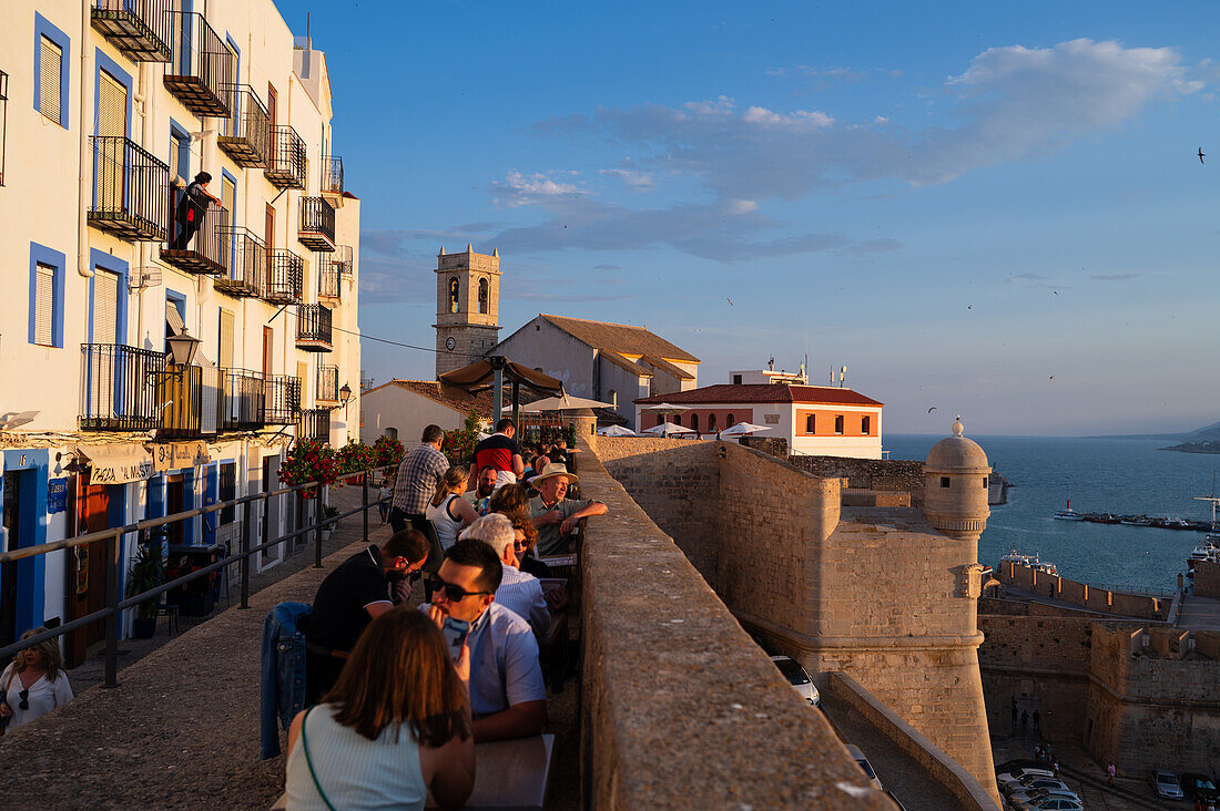 Besucher genießen den Sonnenuntergang von einem Restaurant auf der Stadtmauer der Burg Papa Luna in Peñiscola, Castellon, Valencianische Gemeinschaft, Spanien