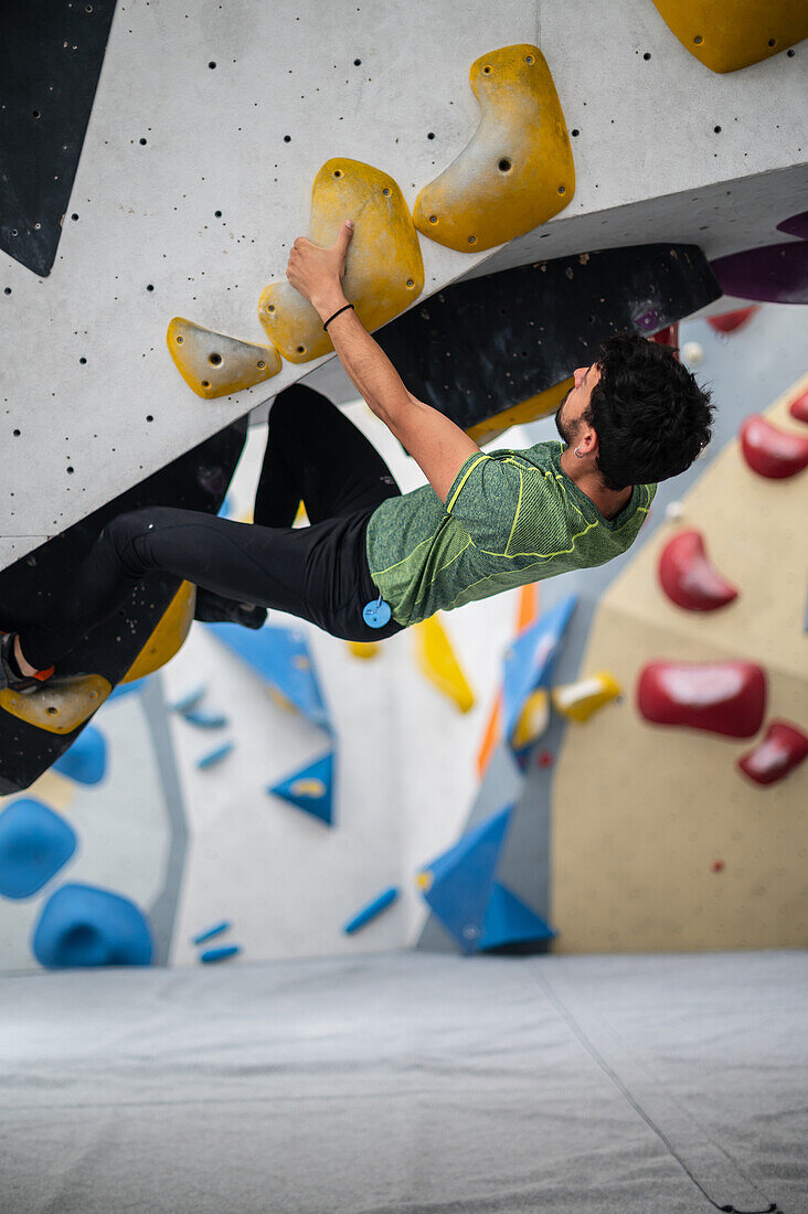 Junger Mann in den Zwanzigern beim Klettern an einer Kletterwand in einer Halle