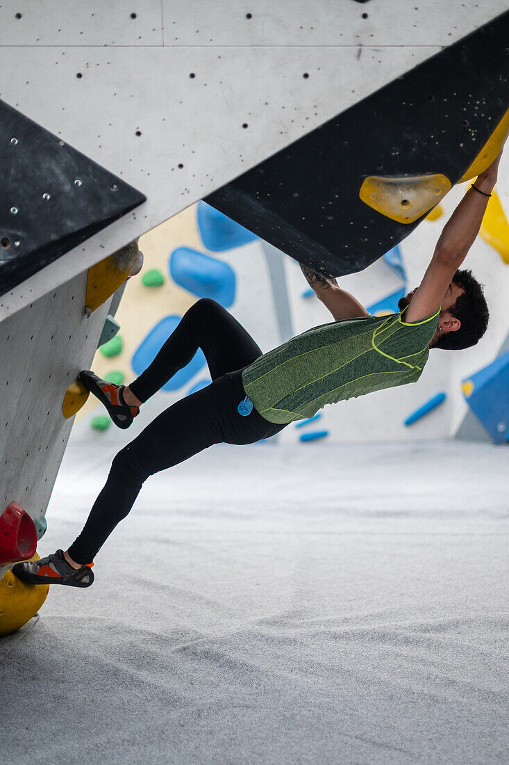 Junger Mann in den Zwanzigern beim Klettern an einer Kletterwand in einer Halle