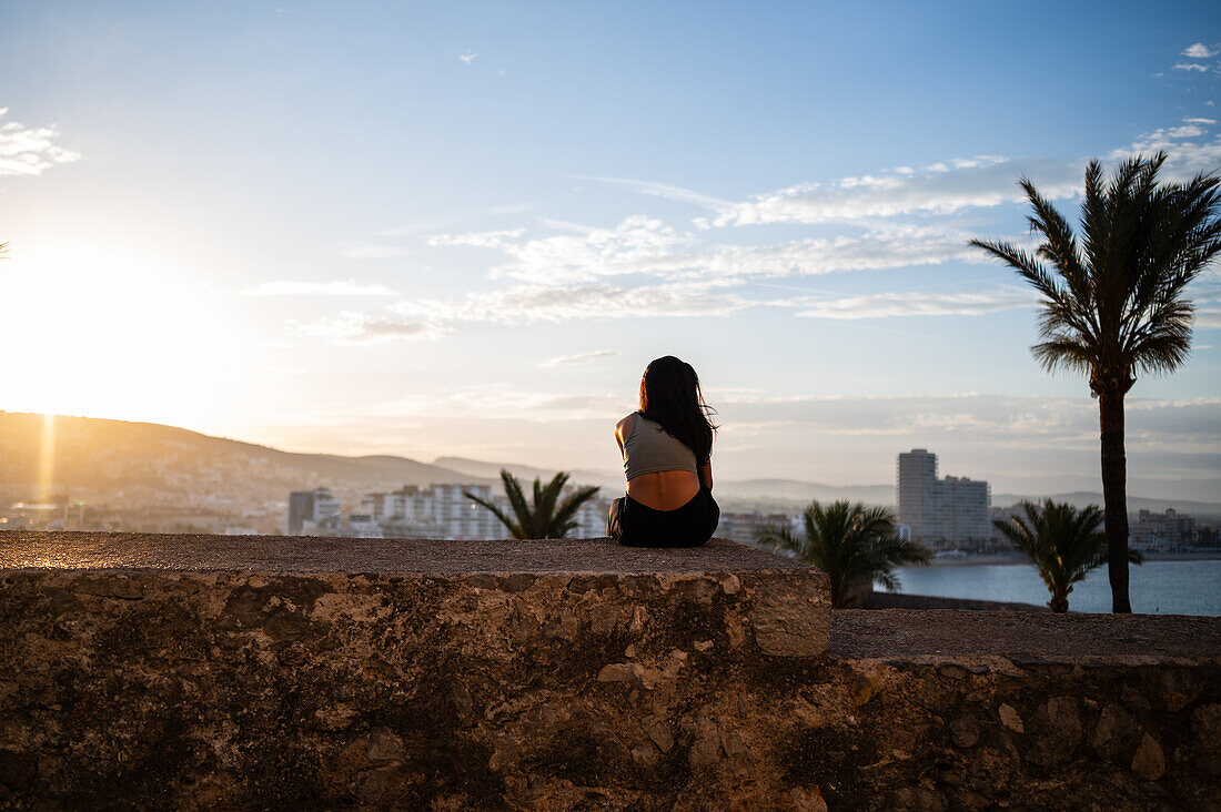 Young woman enjoying the sunset from the city walls of Papa Luna castle in Peñiscola, Castellon, Valencian Community, Spain