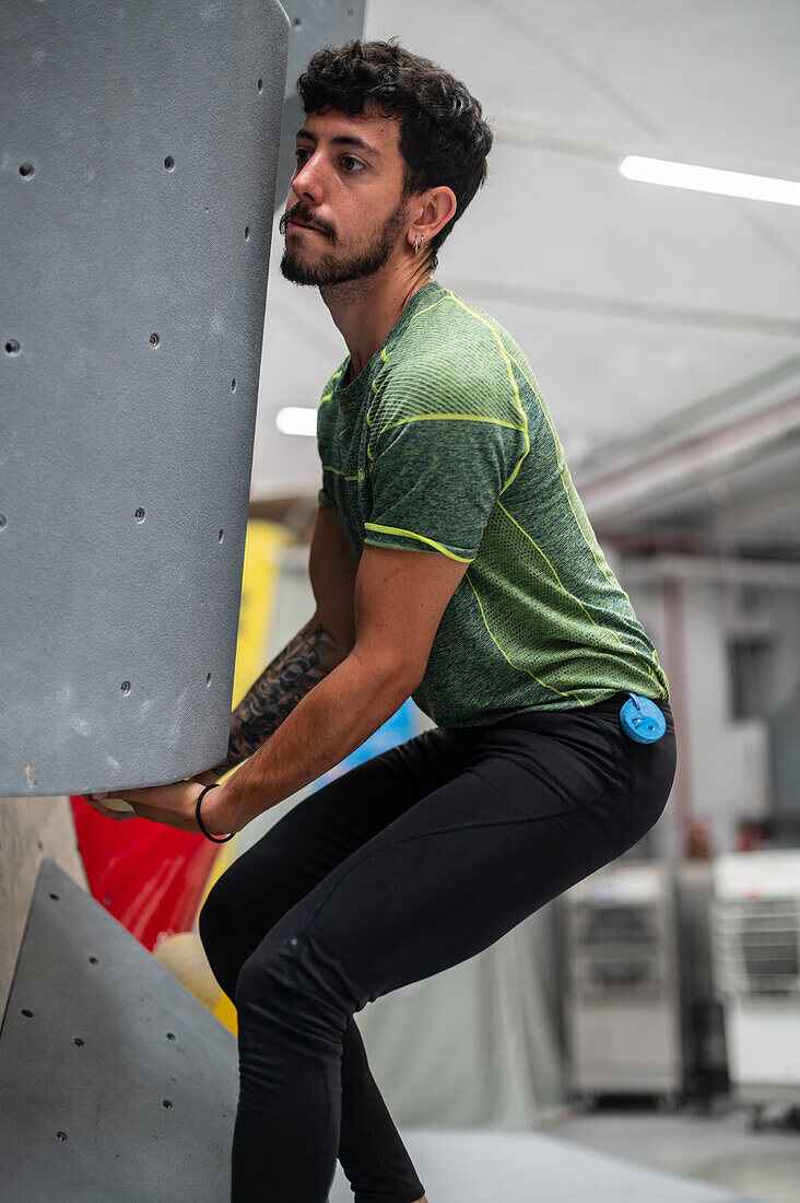 Young man in his twenties climbing on a climbing wall indoors