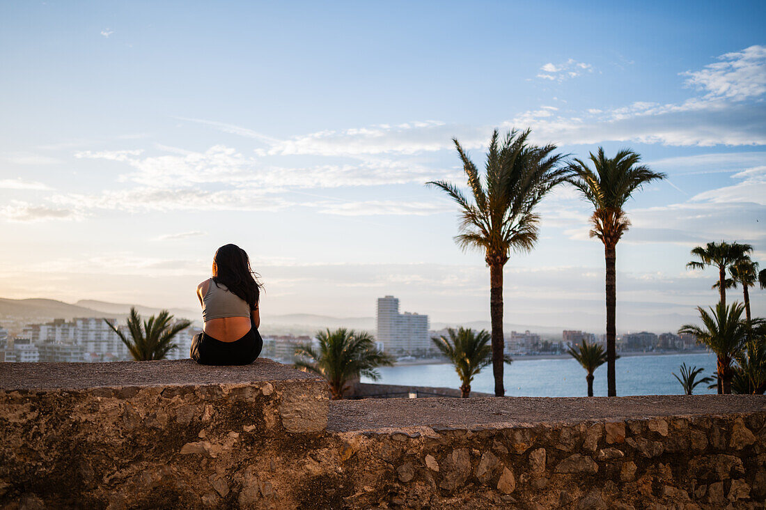 Young woman enjoying the sunset from the city walls of Papa Luna castle in Peñiscola, Castellon, Valencian Community, Spain