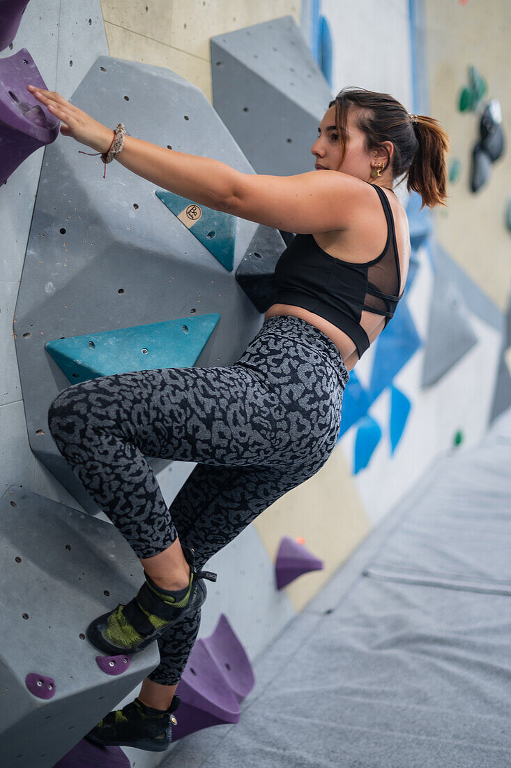 Junger Mann in den Zwanzigern beim Klettern an einer Kletterwand in einer Halle