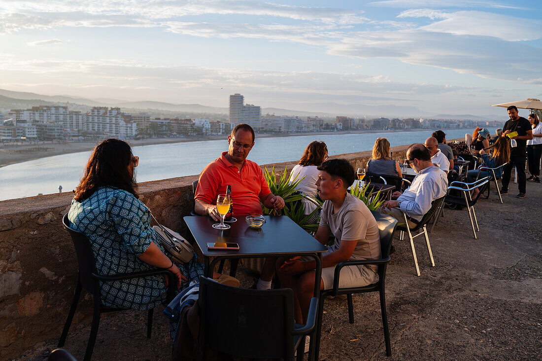 Visitors enjoying the sunset from a restaurant on the city walls of the Papa Luna castle in Peñiscola, Castellon, Valencian Community, Spain