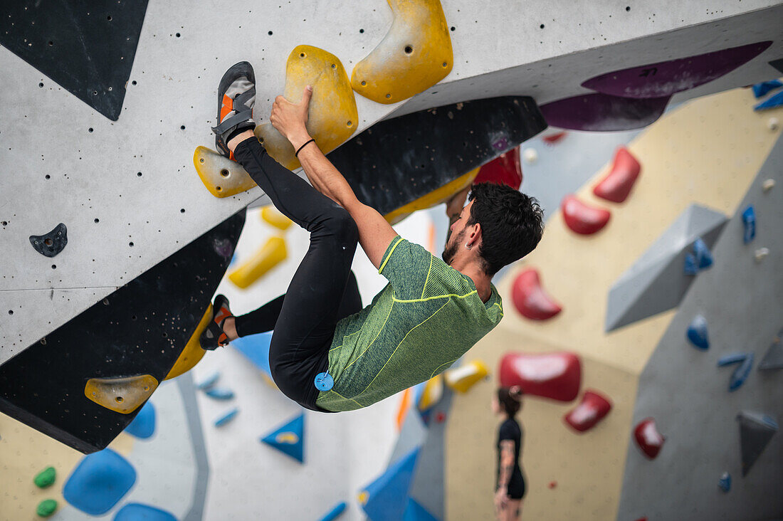 Junger Mann in den Zwanzigern beim Klettern an einer Kletterwand in einer Halle