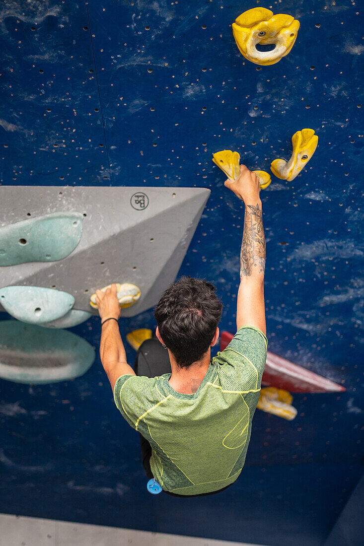 Young man in his twenties climbing on a climbing wall indoors