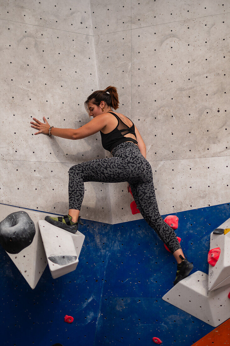 Young man in her twenties climbing on a climbing wall indoors