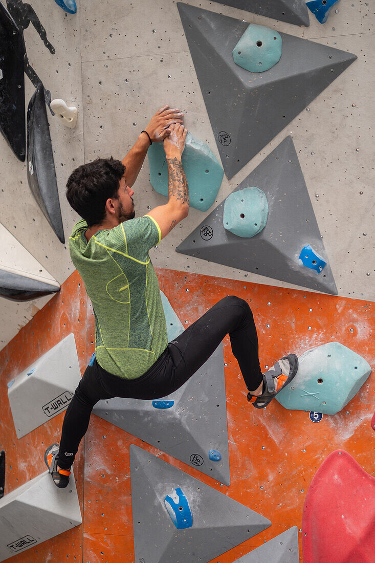 Junger Mann in den Zwanzigern beim Klettern an einer Kletterwand in einer Halle