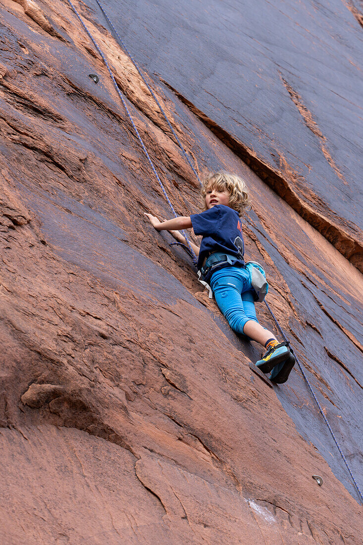 Ein 6-jähriger Junge lernt im Hunter Canyon in der Nähe von Moab, Utah, das Klettern.