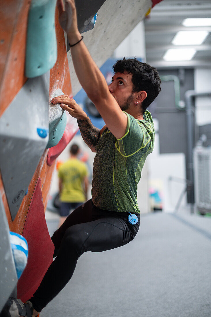 Junger Mann in den Zwanzigern beim Klettern an einer Kletterwand in einer Halle