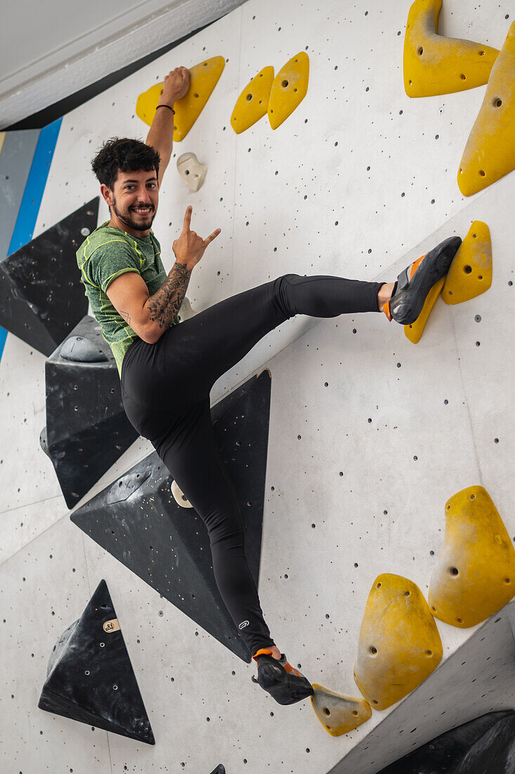 Junger Mann in den Zwanzigern beim Klettern an einer Kletterwand in einer Halle