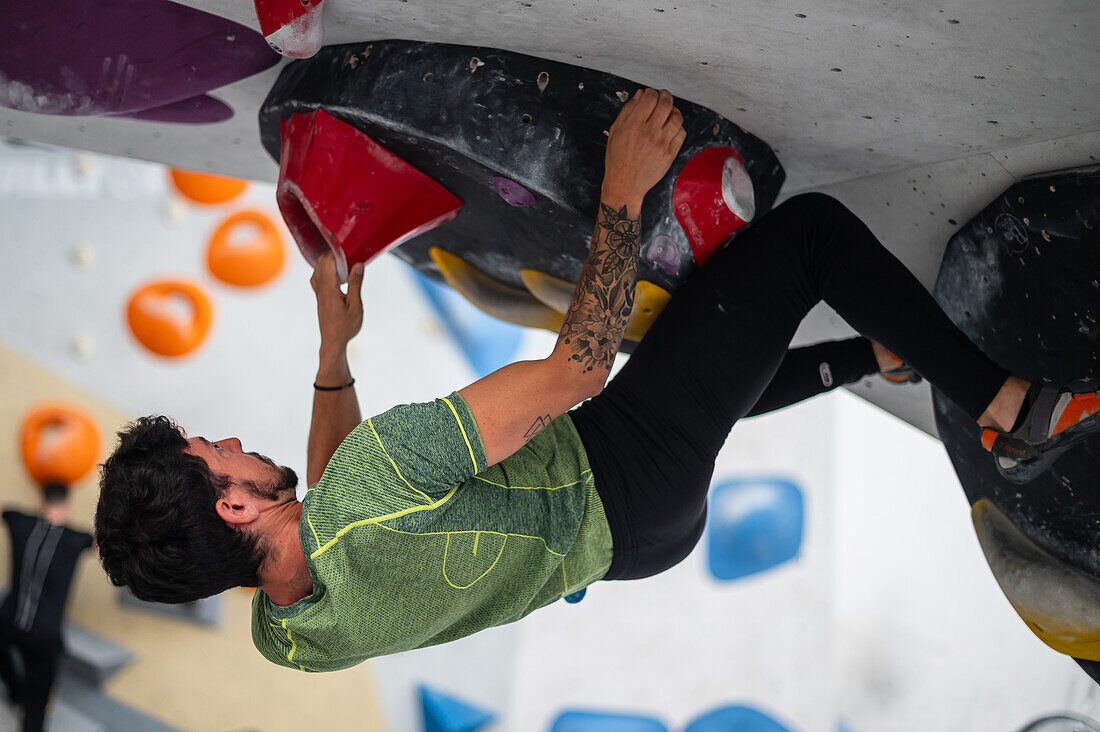 Junger Mann in den Zwanzigern beim Klettern an einer Kletterwand in einer Halle