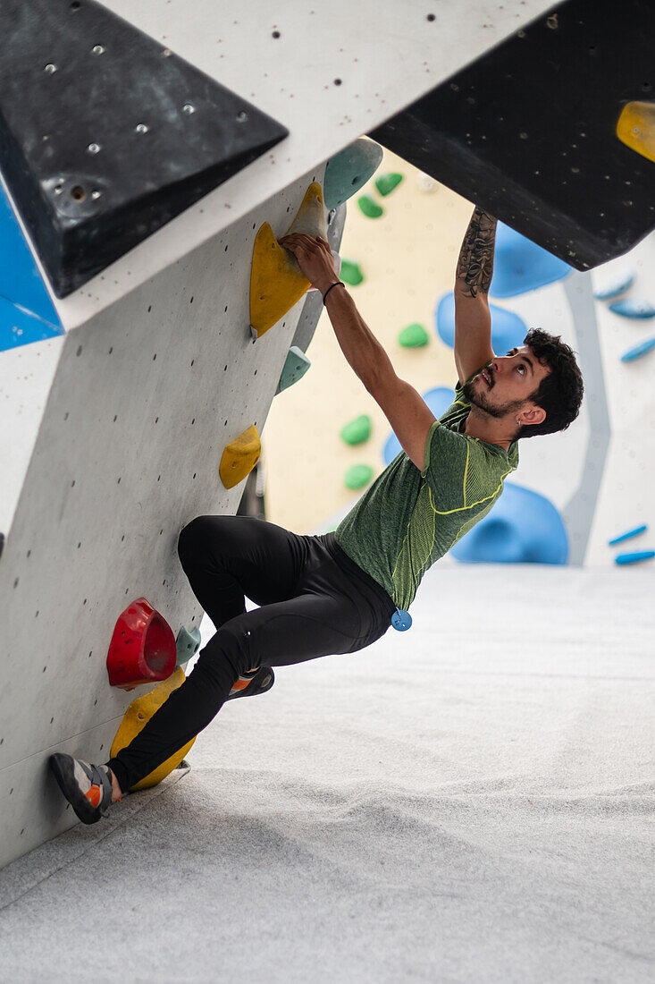 Young man in his twenties climbing on a climbing wall indoors