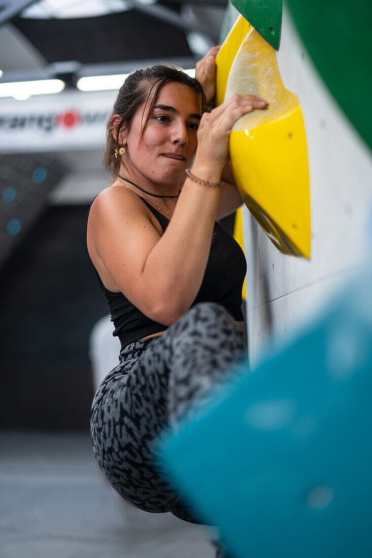 Young man in her twenties climbing on a climbing wall indoors