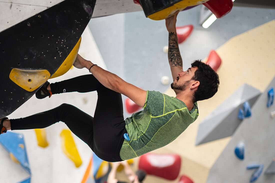 Junger Mann in den Zwanzigern beim Klettern an einer Kletterwand in einer Halle