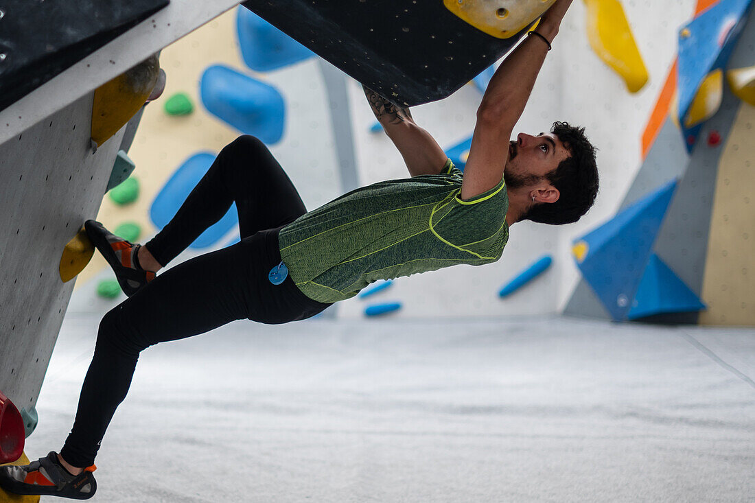 Junger Mann in den Zwanzigern beim Klettern an einer Kletterwand in einer Halle