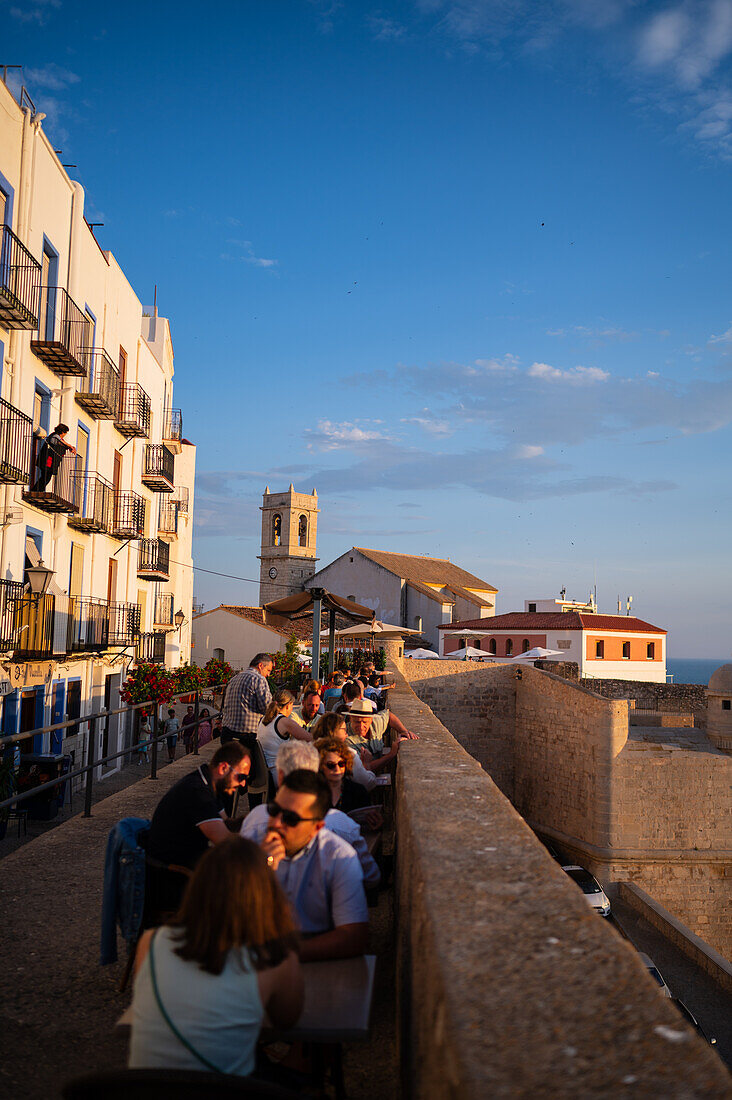 Besucher genießen den Sonnenuntergang von einem Restaurant auf der Stadtmauer der Burg Papa Luna in Peñiscola, Castellon, Valencianische Gemeinschaft, Spanien