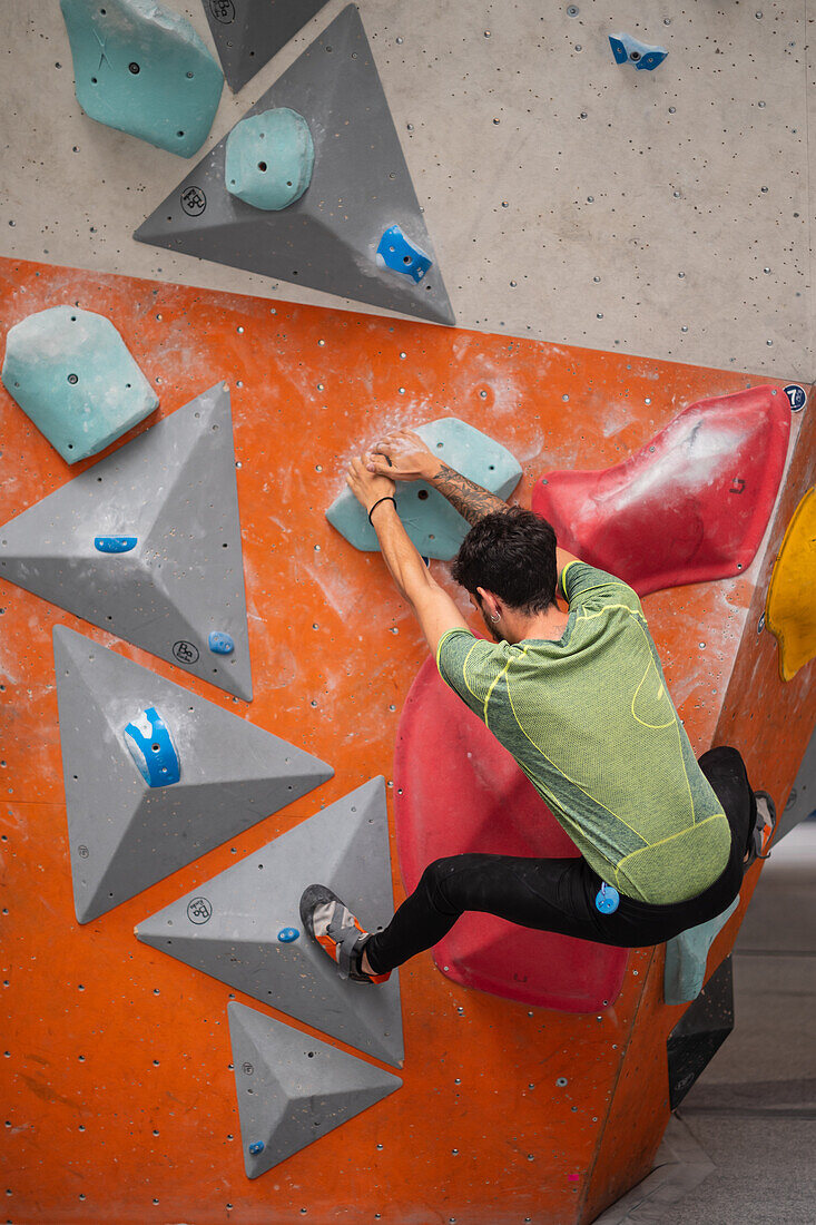 Young man in his twenties climbing on a climbing wall indoors