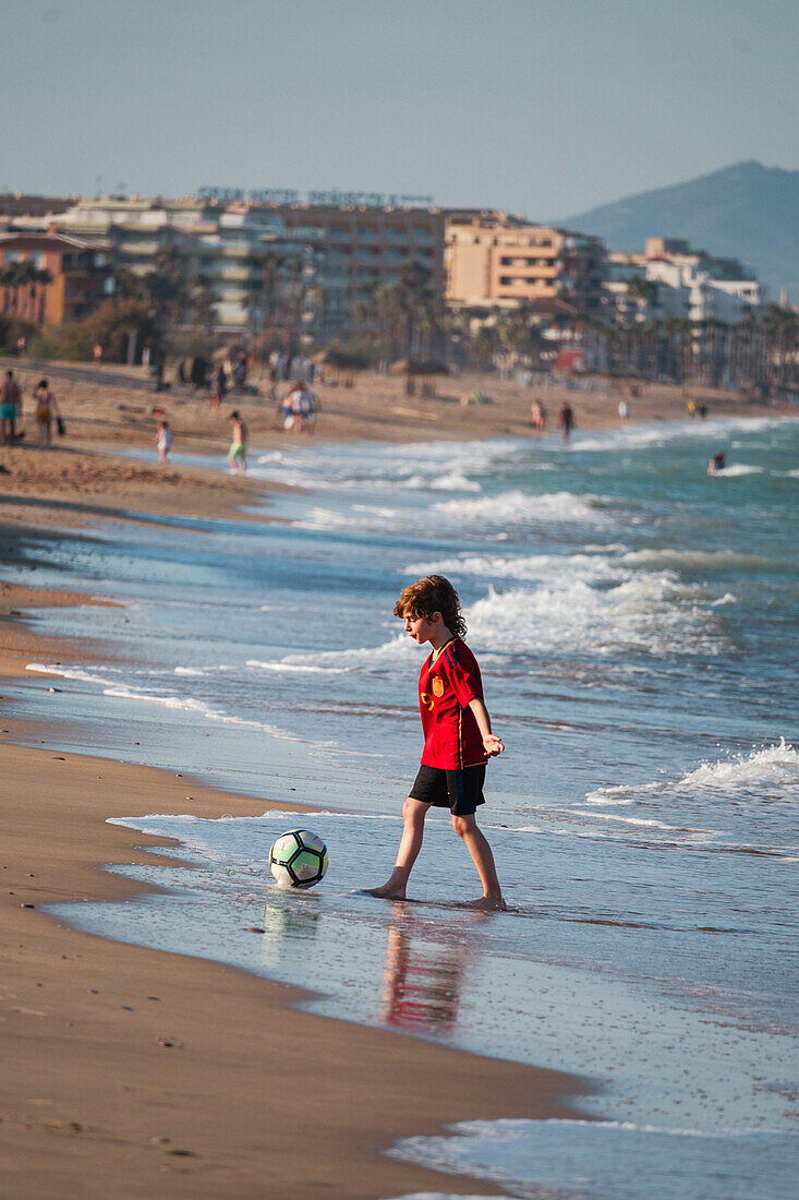 Kleiner Junge spielt mit einem Ball am Strand von Peñiscola, Castellon, Valencianische Gemeinschaft, Spanien