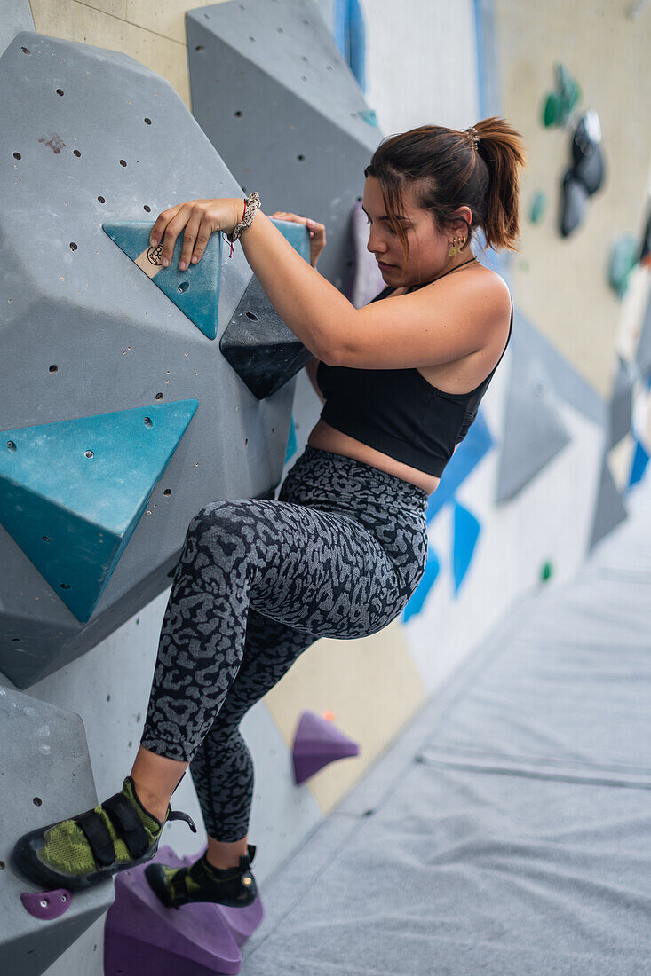 Young man in her twenties climbing on a climbing wall indoors