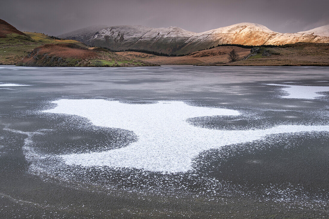 Eismuster auf dem gefrorenen Llyn y Dywarchen mit Foel Goch und Foel Gronin im Winter, Snowdonia National Park (Eryri), Nordwales, Vereinigtes Königreich, Europa