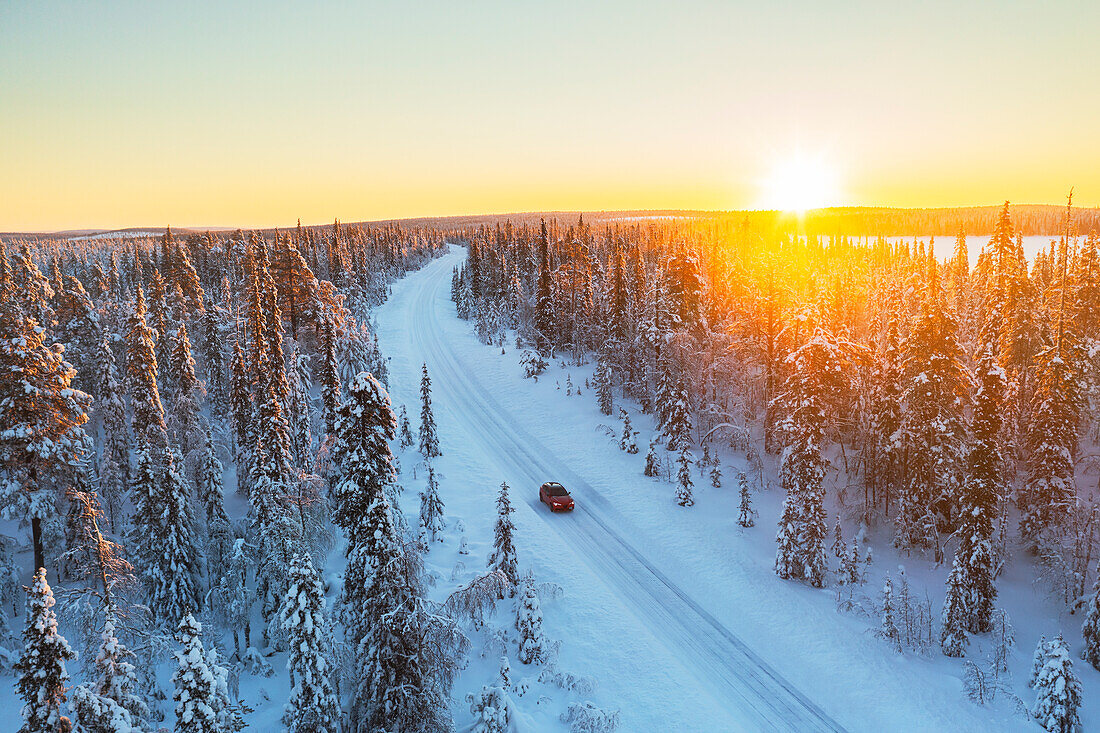 Auto fährt auf der eisigen und leeren Straße durch den borealen verschneiten Wald bei Sonnenaufgang, Schwedisch-Lappland, Schweden, Skandinavien, Europa