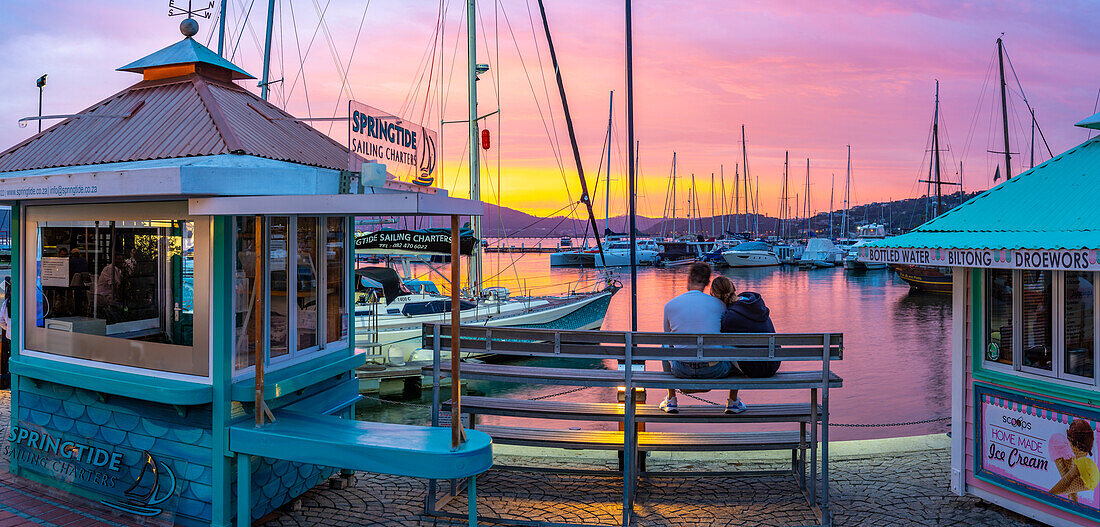 Blick auf ein Paar, das den goldenen Sonnenuntergang an der Knysna Waterfront beobachtet, Knysna, Westliche Kap-Provinz, Südafrika, Afrika