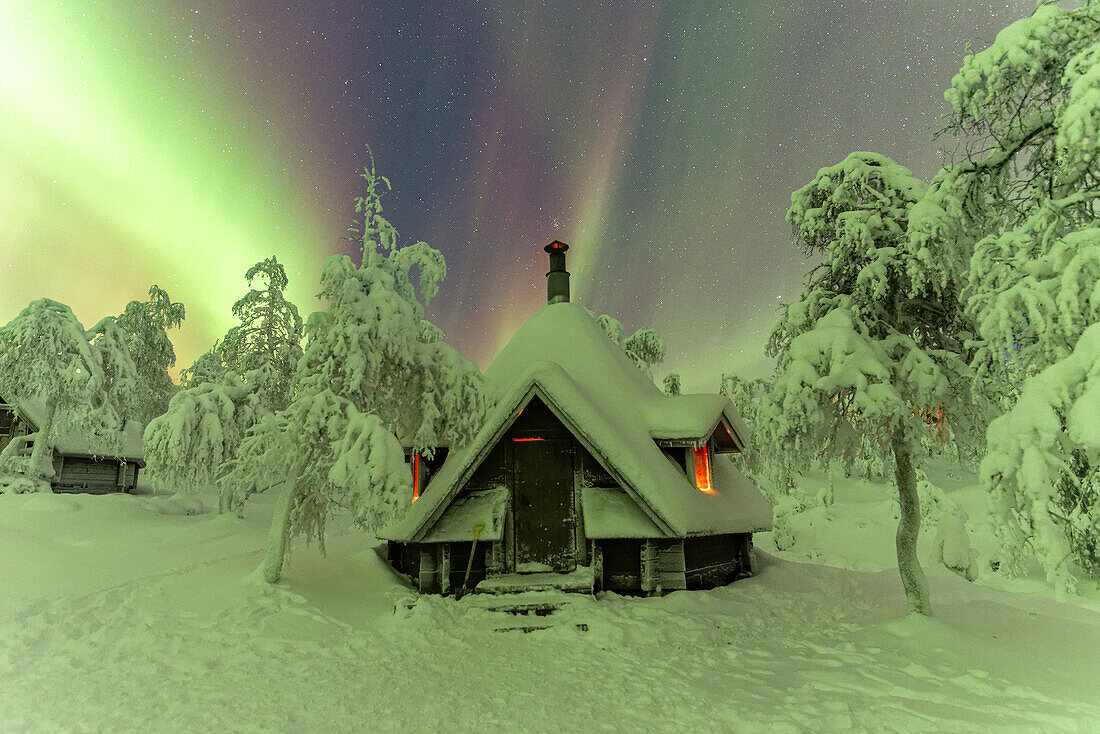 Nordlicht (Aurora Borealis) am Sternenhimmel über einer Berghütte im schneebedeckten Wald von Finnisch-Lappland, Pallas-Yllastunturi-Nationalpark, Muonio, Finnisch-Lappland, Finnland, Skandinavien, Europa