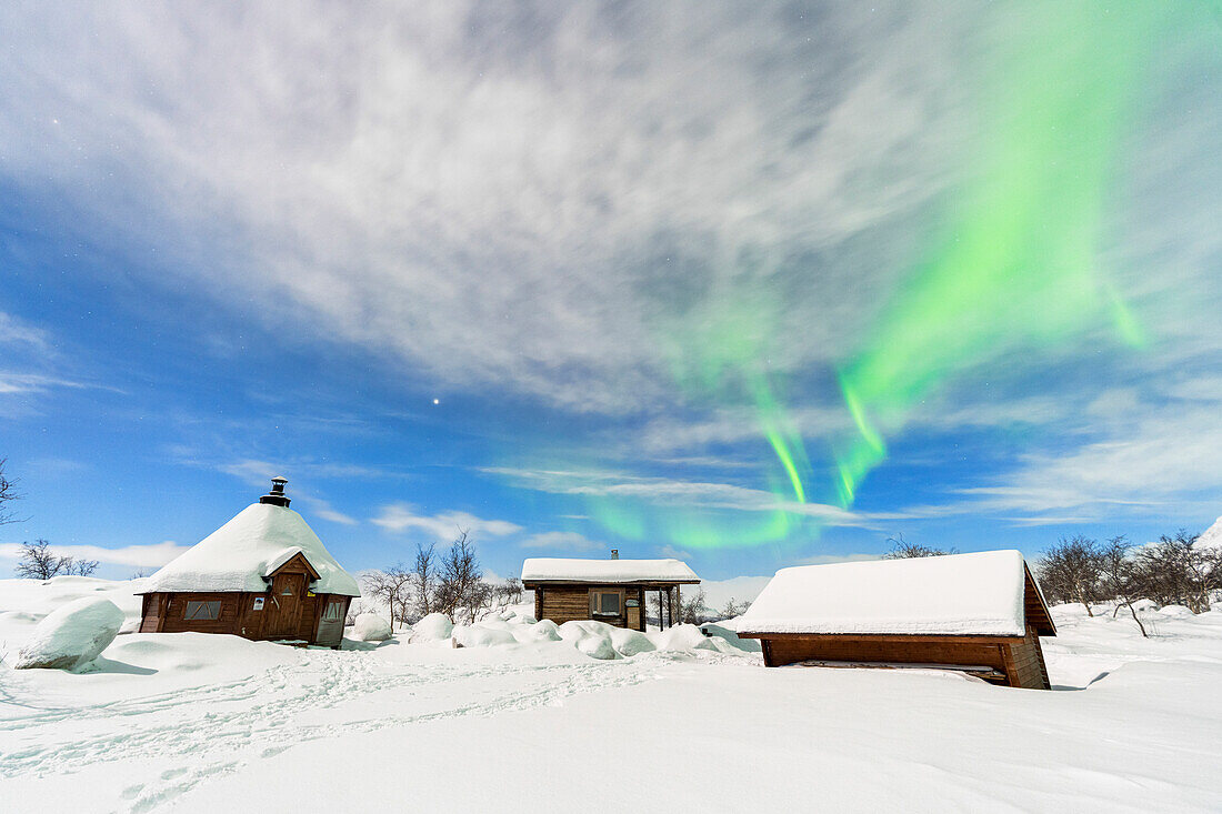 Typische Holzhäuser mit Schnee bedeckt unter dem Nordlicht (Aurora Borealis), Vollmondnacht, Kilpisjarvi, Gemeinde Enontekio, Finnisch-Lappland, Finnland, Skandinavien, Europa