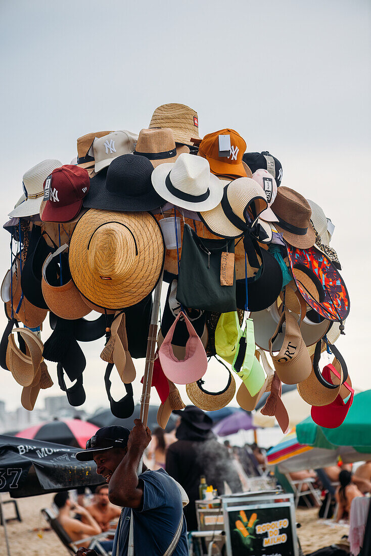 Salesman displaying hats for sale, at Leblon beach in Rio de Janeiro, Brazil, South America