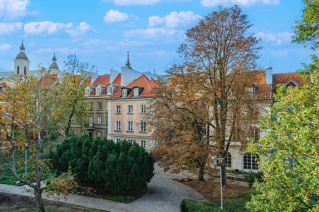 Blick auf traditionelle niedrige Dachziegelhäuser hinter einer Parkanlage unter blauem Himmel mit Wolken, Warschau, Polen, Europa