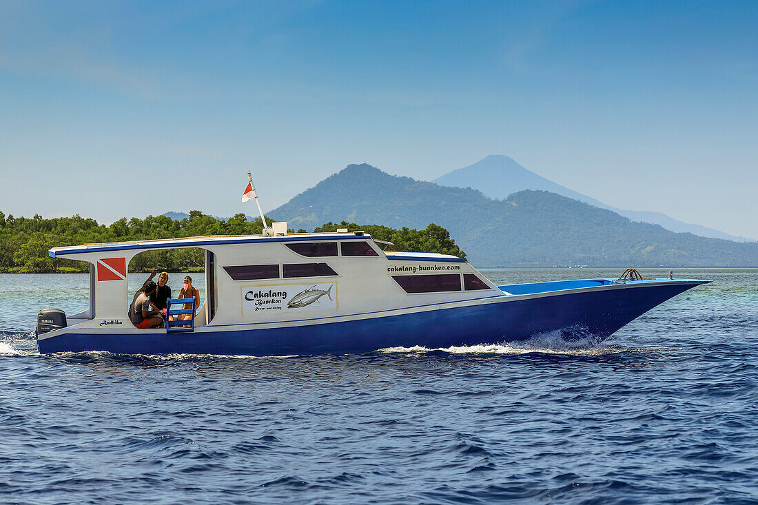 Tauchboot mit dem Festland und der Insel Manadotua dahinter, vor dieser korallengesäumten Urlaubs- und Tauchinsel. Bunaken, Nordsulawesi, Indonesien, Südostasien, Asien