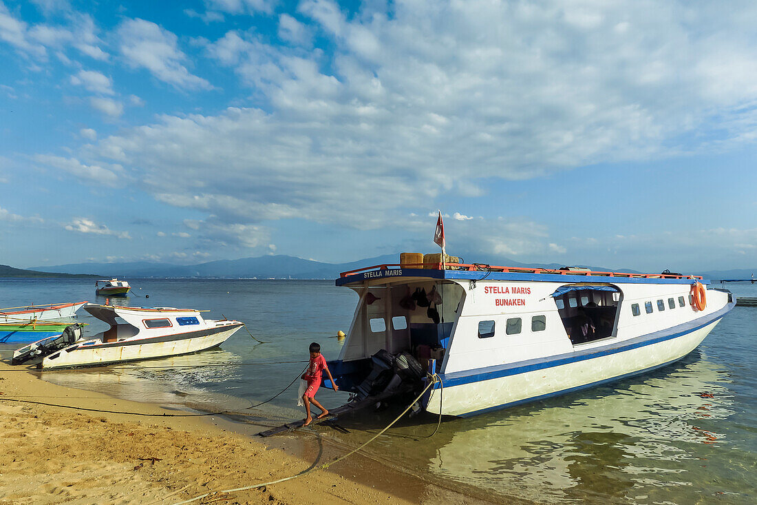 Ein Junge verlässt die Fähre auf dieser beliebten, von Korallen gesäumten Ferieninsel und Tauchdestination. Bunaken, Nordsulawesi, Indonesien, Südostasien, Asien