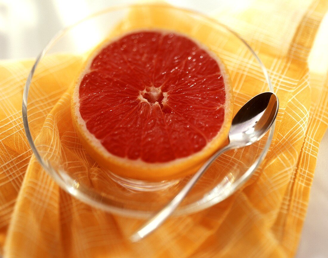 Pink grapefruit half with spoon on glass plate