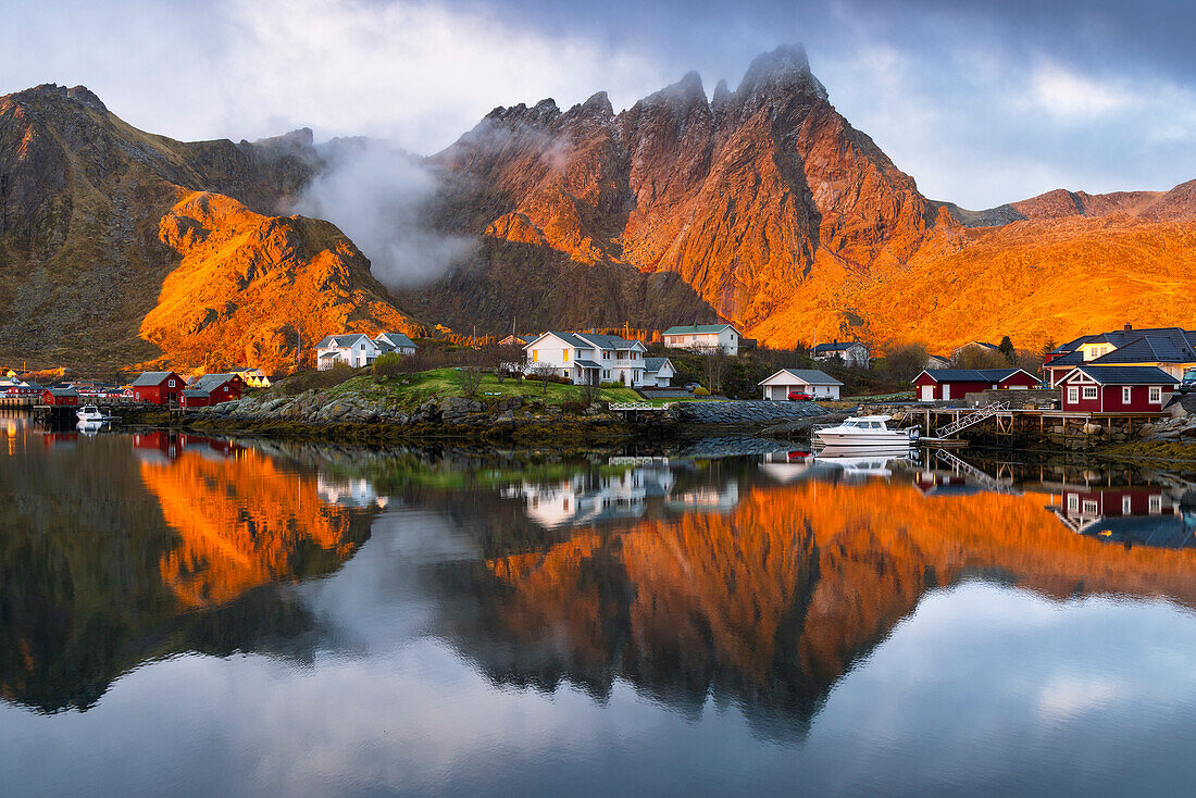 Reflections of houses and mountains in the water at Ballstad village during sunrise, Vestvagoy, Nordland, Lofoten Islands, Norway, Europe