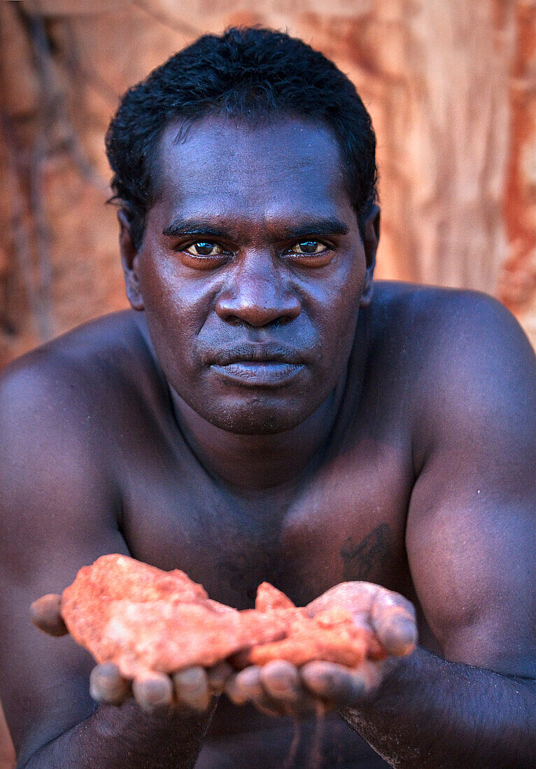 Porträt, Aborigine-Mann, der einen alten roten Felsen in der Nähe von Bawaka Homeland hält, Ost Arnhem Land, Northern Territory, Australien, Pazifik