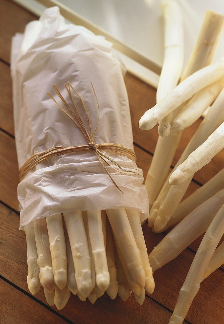 White asparagus wrapped in paper on wooden background