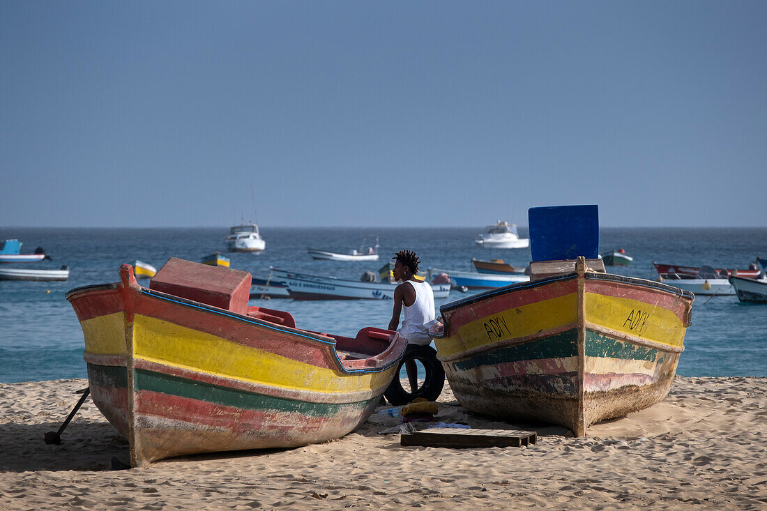 Einheimischer ruht sich zwischen bunten Fischerbooten am Strand Praia de Santa Maria aus, Santa Maria, Sal, Kapverdische Inseln, Atlantik, Afrika