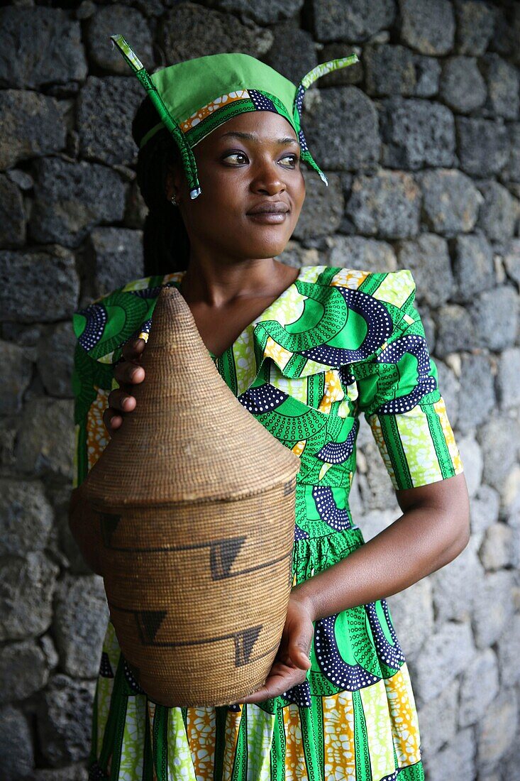 Rwanda, Volcanoes National Park, young Rwandan woman in traditional dress, member of staff of Bisate Lodge, carrying a basketry