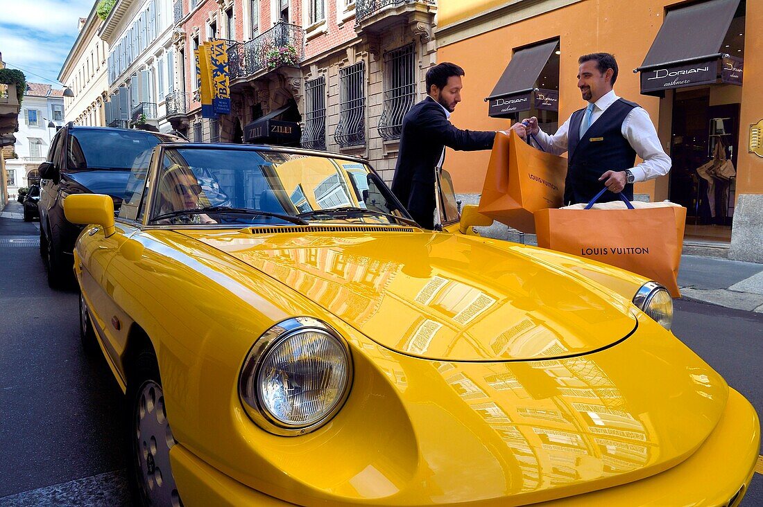 Italy, Lombardy, Milan, Fashion Quadrilateral (Quadrilatero della moda), Alfa Romeo Duetto Spider yellow cabriolet in front of the Four Seasons Hotel Milano, the doorman brings a Vuitton bag