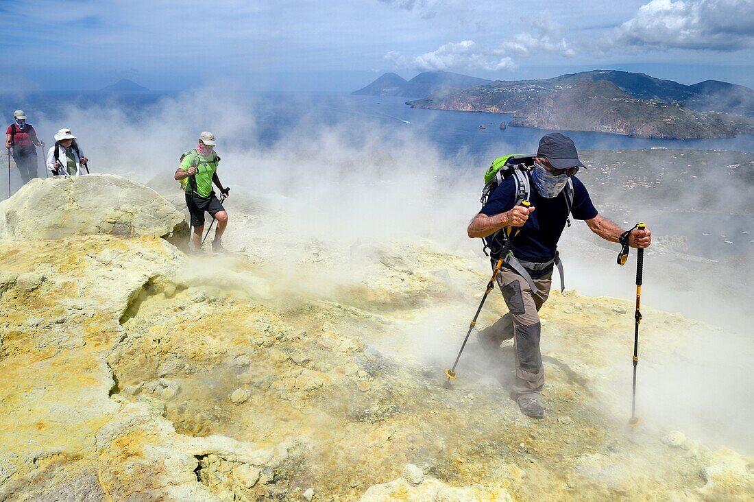 Italien, Sizilien, Äolische Inseln, UNESCO-Welterbe, Insel Vulcano, Wanderer, die den Krater des Vulkans della Fossa durch Schwefelfumarolen besteigen, im Hintergrund die Insel Lipari und dann die Insel Salina