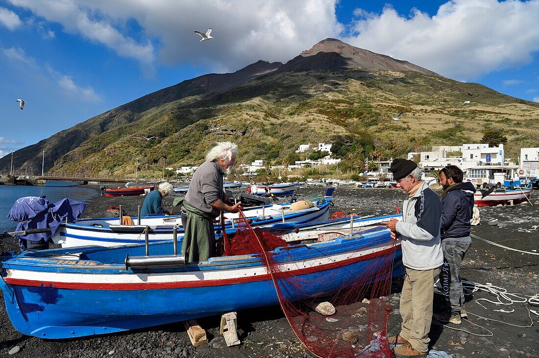 Italien, Sizilien, Äolische Inseln, von der UNESCO zum Weltkulturerbe erklärt, Insel Stromboli, der Fischer Gaetano Cusolito repariert mit seinen beiden Brüdern am Strand von Scari die Netze, im Hintergrund der Vulkan Stromboli