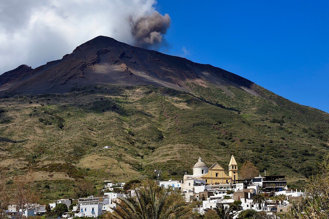 Italien, Sizilien, Äolische Inseln, von der UNESCO zum Weltkulturerbe erklärt, Insel Stromboli, einer der mehrfachen und regelmäßigen Ausbrüche des 924 m hohen Vulkans Stromboli, im Vordergrund die Chiesa di San Vincenzo (St. Vincent Kirche) im Dorf Stromboli