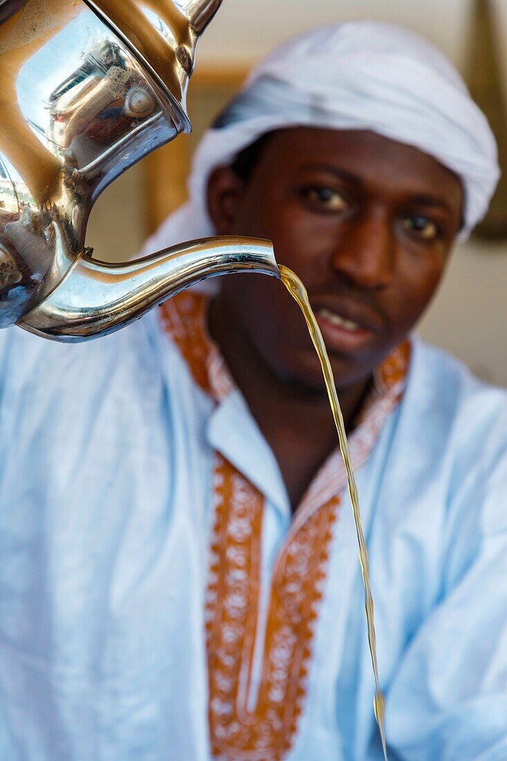 Marocco, Oued Ed-Dahab, Dakhla, Les Dunes Eco-lodge, young Moroccan serving tea under a traditional saharoui tent