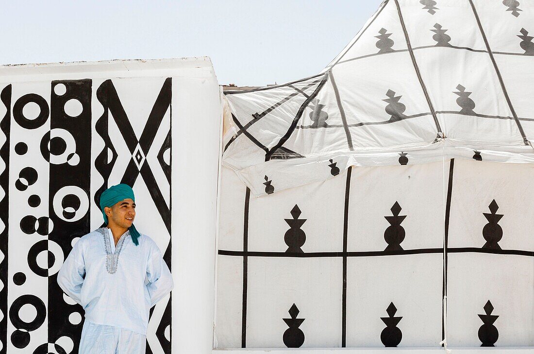 Marocco, Oued Ed-Dahab, Dakhla, Les Dunes Eco-lodge, young Moroccan in traditional clothes in front of a tent decorated with African tribal patterns